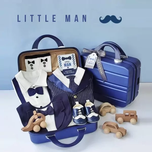 A navy blue suitcase overflowing with a "Little Gentleman" baby gift set, including tiny suits, shoes, and wooden cars.