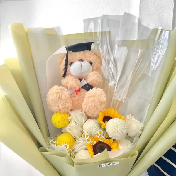 Graduation teddy bear in bouquet with sunflowers and white flowers, wearing a cap.