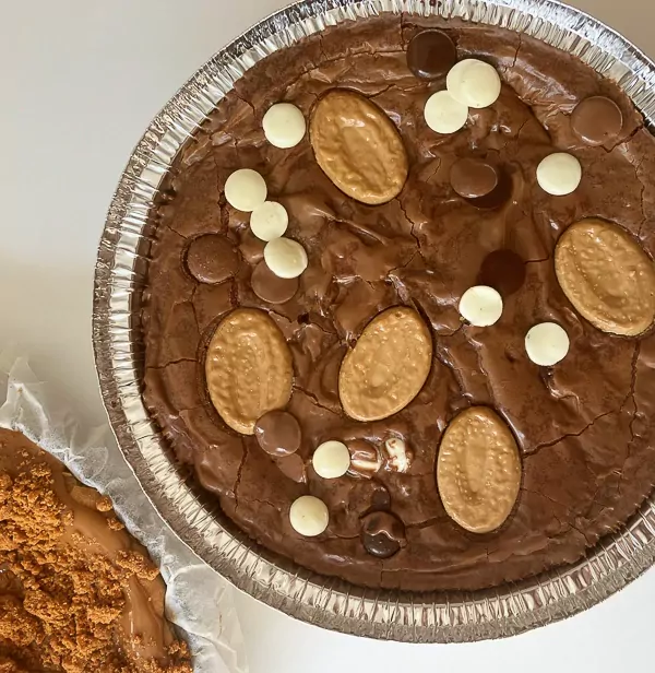 Decadent 6-inch Valrhona chocolate brownie topped with chocolate buttons and cookies in a foil pan.