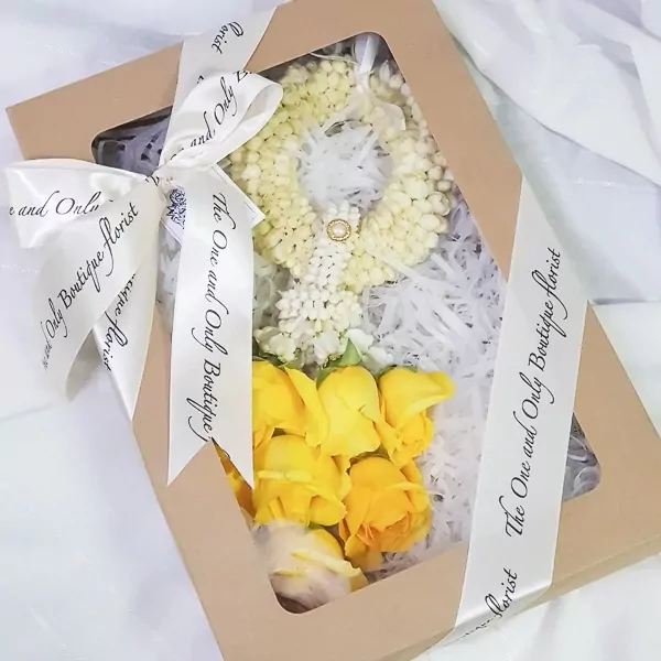 Brown box with white ribbon, white flower garland, and yellow roses inside.