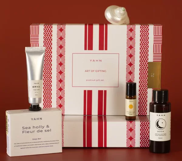 Yahn premium gift set with hand cream, soap bar, perfume roller, and body oil on red background.