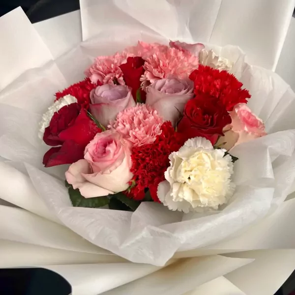 A bouquet of pink, red, and white roses and carnations wrapped in white paper.