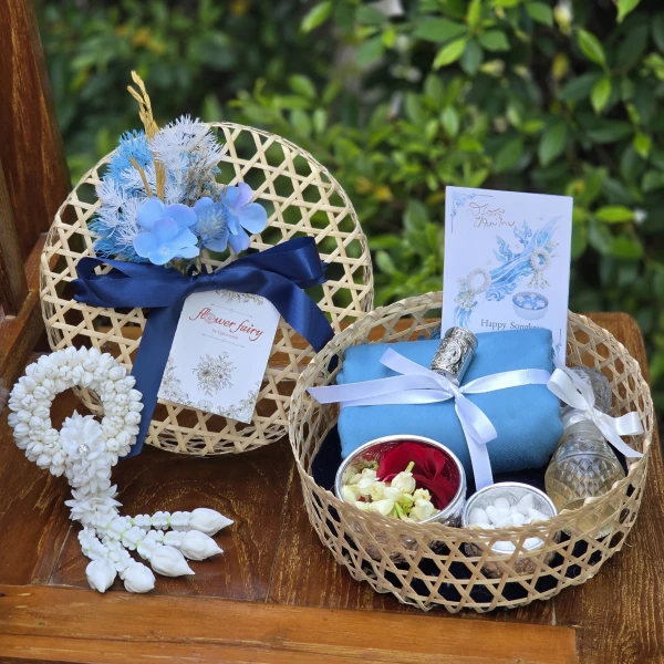 Woven baskets hold blue fabric, flowers, and a jasmine garland, symbolizing Thai New Year traditions.