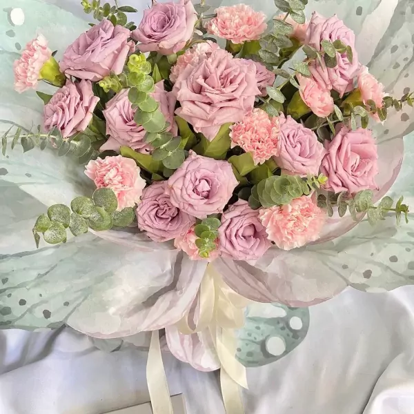 Bouquet of pink roses and carnations with eucalyptus leaves, wrapped in light green paper with butterfly designs.