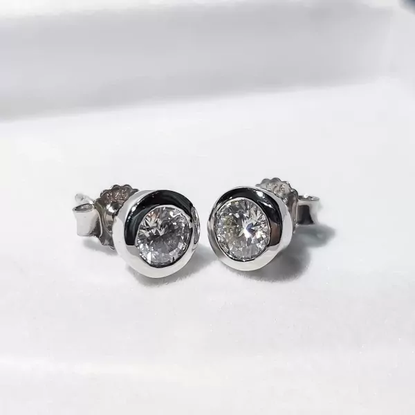 Pair of white gold stud earrings with round-cut moissanite diamonds in a bezel setting.