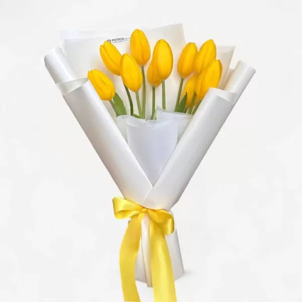 A bouquet of yellow tulips wrapped in white paper and tied with a yellow ribbon.