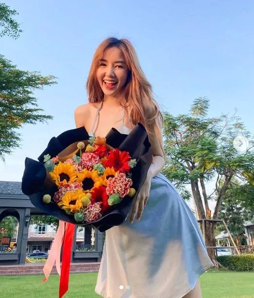 Woman smiles holding a "Partner In Crime" bouquet of sunflowers, gerberas, and carnations.