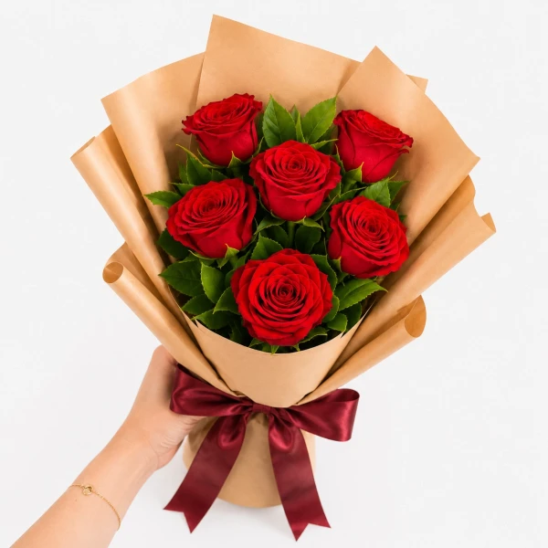 Woman holding a bouquet of six red roses wrapped in brown paper with a red ribbon.