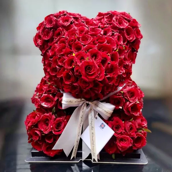 A teddy bear made of red roses, tied with a ribbon and gift tag.