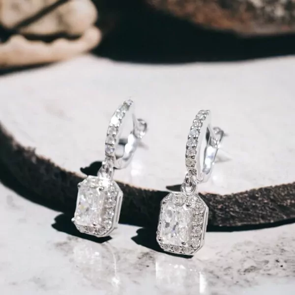 Silver drop earrings with two large emerald-cut moissanite diamonds surrounded by smaller stones.