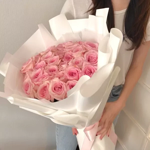 Bouquet of 30 pink roses beautifully wrapped in white paper, held by a person.