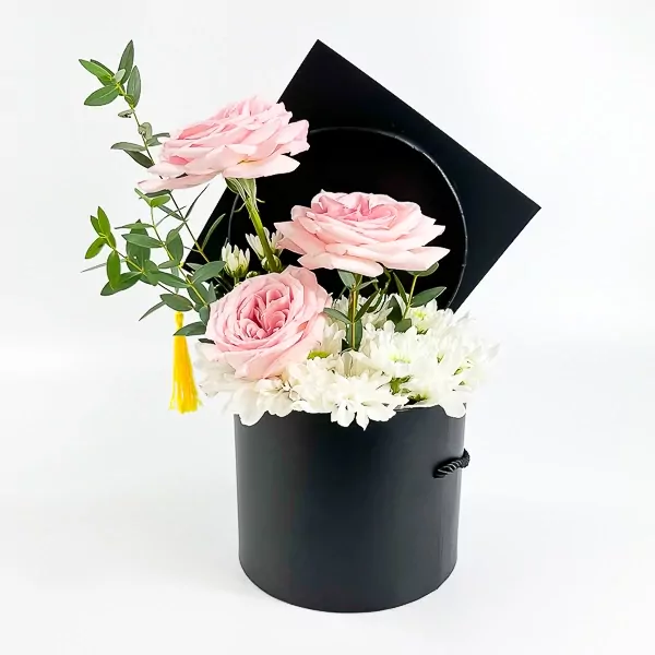 Black graduation box with pink roses, white mums, and a yellow tassel.