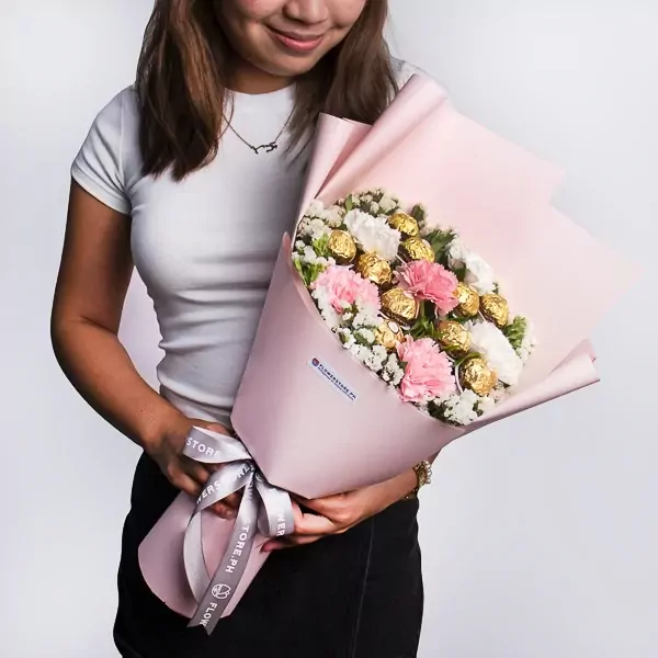 Woman holding pink bouquet with pink and white carnations, white statice, and Ferrero Rocher chocolates.