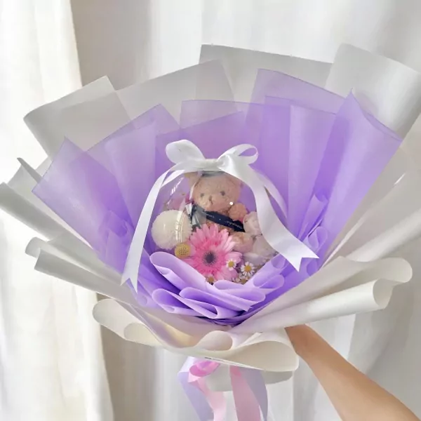 Graduation bouquet with teddy bear in clear balloon, surrounded by purple and white wrapping.