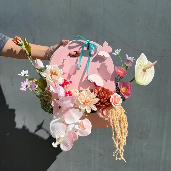 Pink butterfly bloom box with assorted artificial flowers and a ribbon handle.