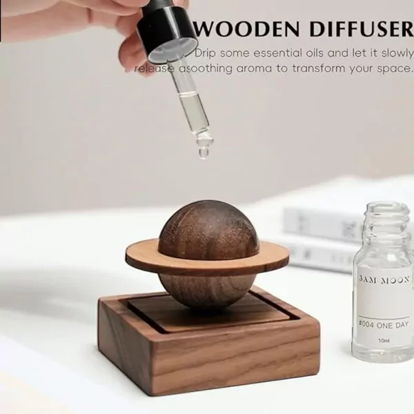 Wooden planet diffuser with dropper adding oil, beside a small bottle.