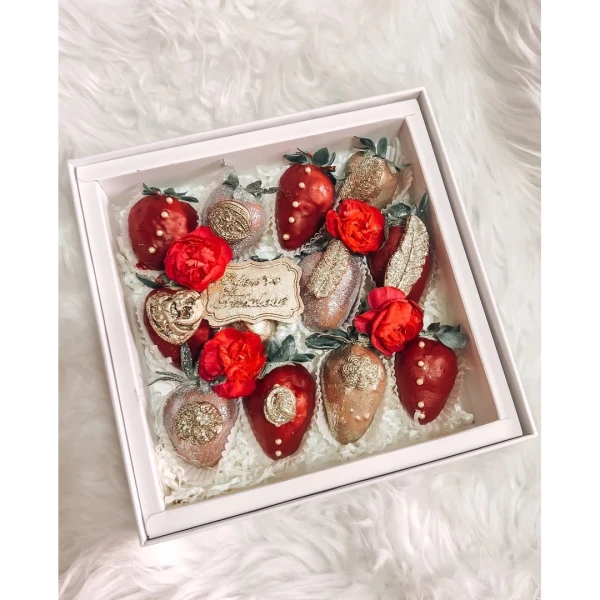 Box of chocolate-dipped strawberries with red flowers and gold embellishments.