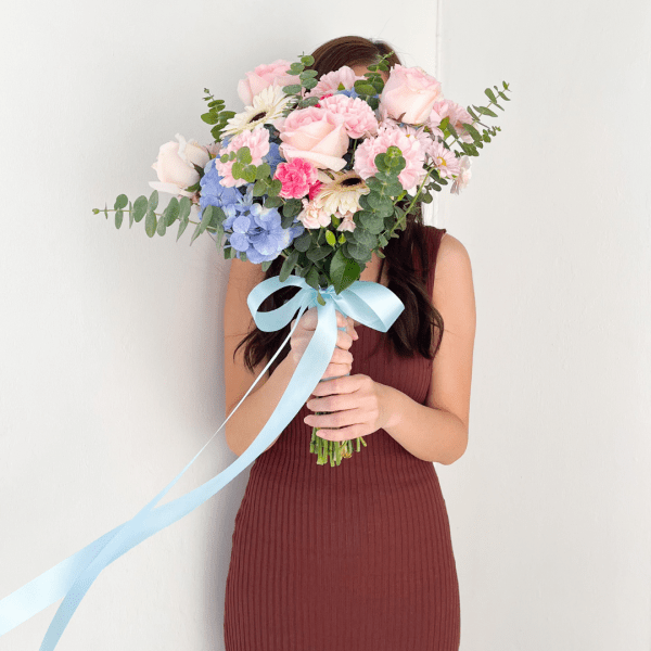 Woman holding a large Juliet wedding bouquet with pink roses, hydrangeas, and blue ribbons.