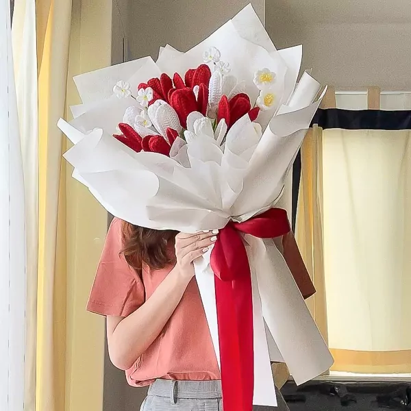 Crocheted red and white tulips bouquet with red ribbon, held by a person.