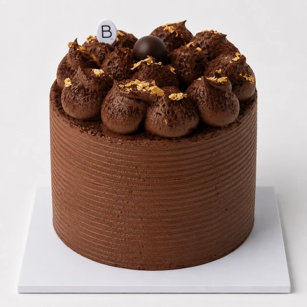A round chocolate fudge cake with swirls of chocolate frosting, truffles, and gold leaf.