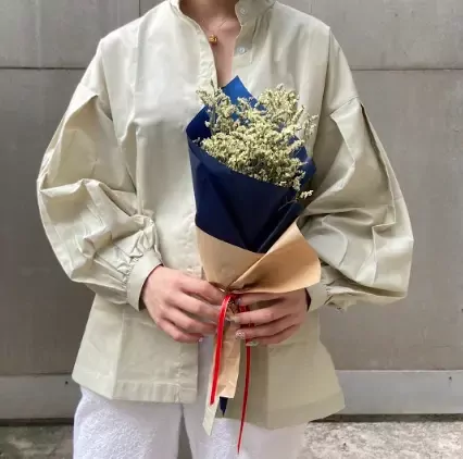 Person holding a mini-bouquet of yellow limonium flowers wrapped in craft and navy paper.