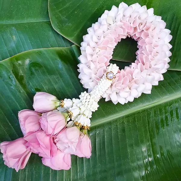 Garland of pink and white flowers with pearl accent on banana leaves.