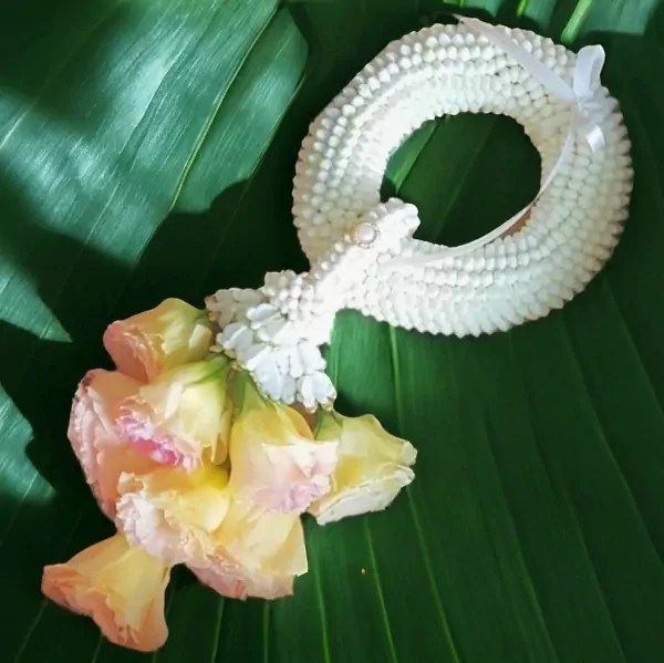 A white flower garland with yellow and pink flowers on green leaves.
