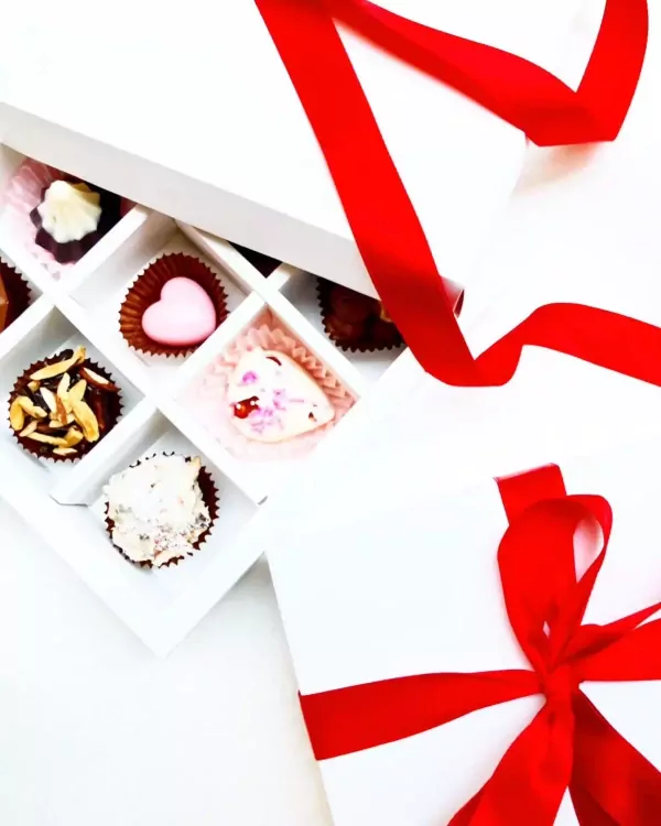 Box of assorted chocolates with red ribbon, featuring heart-shaped, almond-topped, and white chocolates.