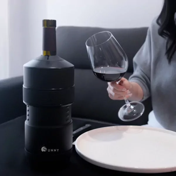A black Sunny Wine Chiller sits next to a glass of red wine and a white plate.