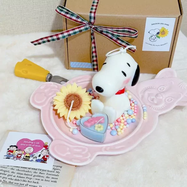Snoopy and sunflower scented candles on a pink tray with a gift box.