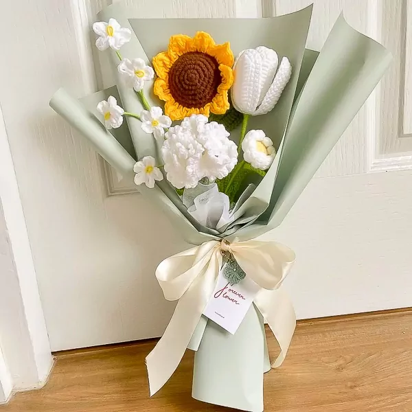 Crocheted bouquet with a sunflower, tulip, daisies, and carnations, wrapped in pale green paper with a cream ribbon.
