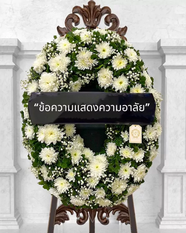 White chrysanthemum wreath with "Condolence message" ribbon, on a dark ornate stand.