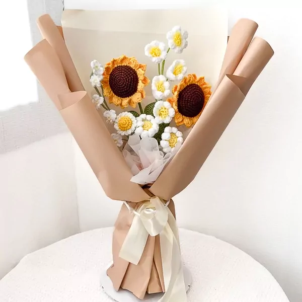 Crocheted sunflowers and white daisies in a tan paper bouquet tied with a cream ribbon.