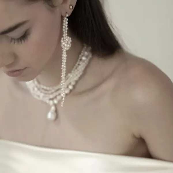 Woman wearing a multi-strand pearl necklace with baroque drop pendant and long pearl drop earrings.