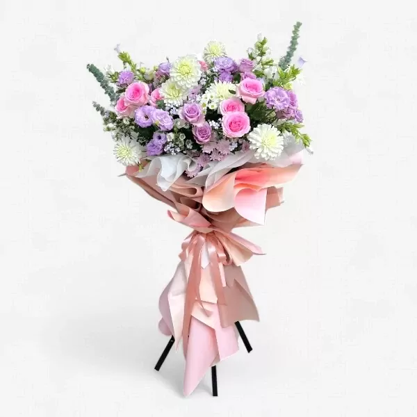 A tall floral stand with pink, purple, and white flowers, wrapped in pastel pink and peach paper.