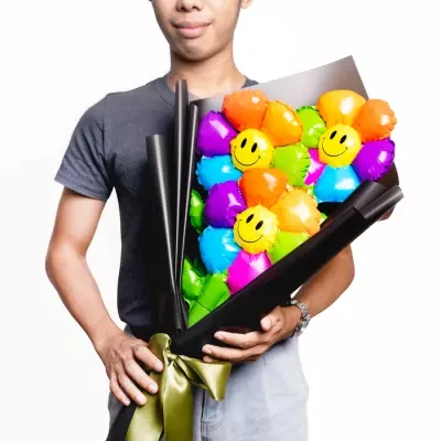 Man holding a bouquet of colorful smiley face balloons wrapped in black paper and tied with a green ribbon.