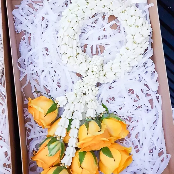Yellow roses and a white flower garland in a box with white shred filler.