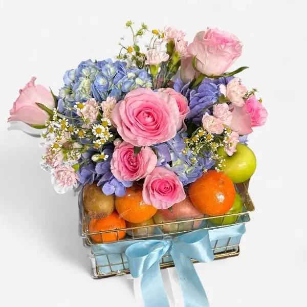 Fruit basket with pink roses, blue hydrangeas, oranges, kiwis, and apples, tied with a blue ribbon.