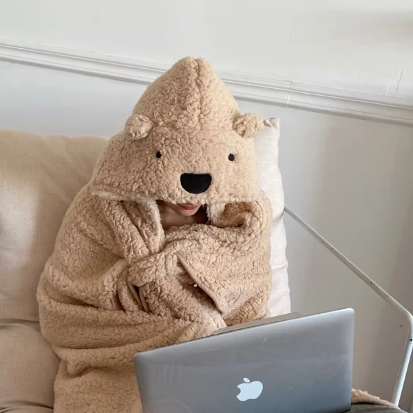 Person in fuzzy bear hoodie blanket using a laptop.