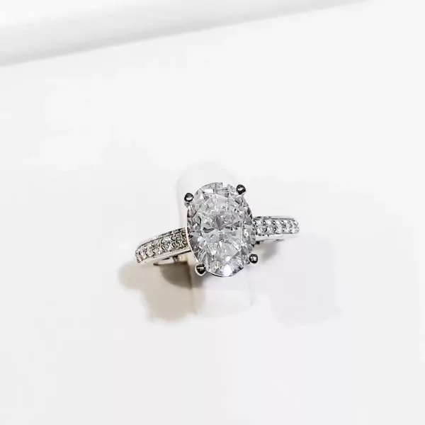 Oval-cut moissanite diamond ring with pavé band on white background.
