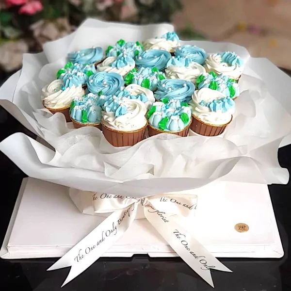 Cupcake bouquet with blue, white, and green frosting in brown wrappers, presented in white tissue paper and a white box with ribbon.