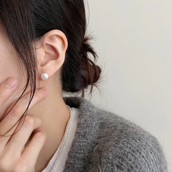 Close-up of a woman's ear wearing a single 8mm round pearl stud earring.