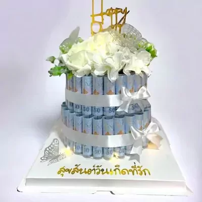 Two-tiered cake decorated with rolled Thai 50 baht banknotes and white flowers.