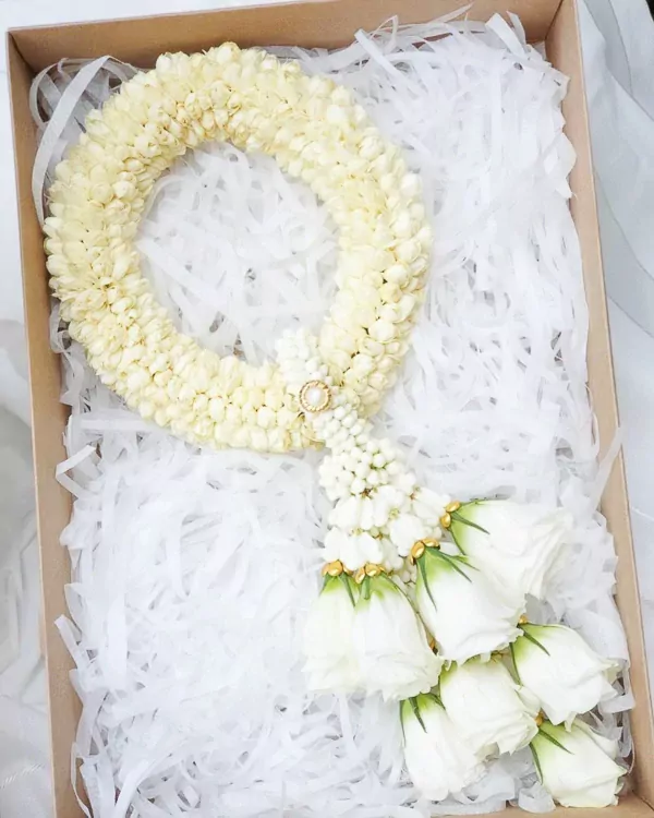 A white jasmine flower garland with white roses and a pearl embellishment in a gift box.