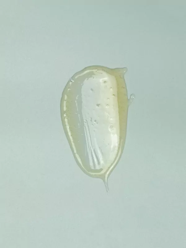 A dollop of translucent yellow body wash with small air bubbles on a light blue background.
