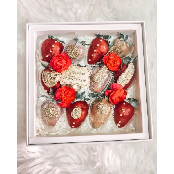 Chocolate-dipped strawberries with gold glitter and red roses in a gift box.