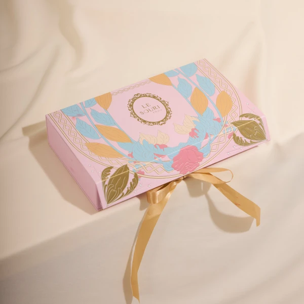 Pink gift box with floral design and gold ribbon, featuring "LE SOURI" logo.