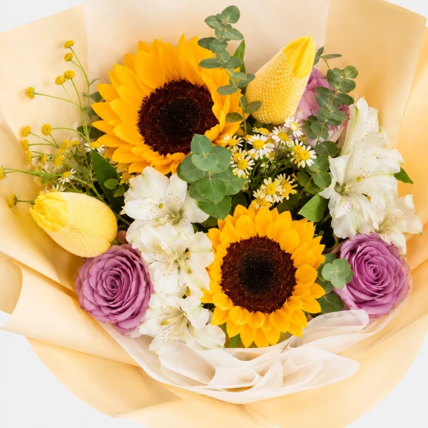 Bouquet of sunflowers, purple roses, white flowers, and yellow tulips wrapped in yellow paper with a yellow bow.
