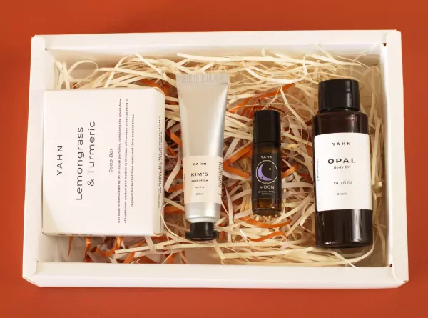 A white gift box filled with YAHN lemongrass & turmeric soap, hand cream, roll-on perfume, and body oil.