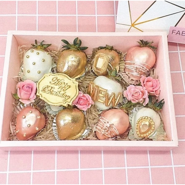 A pink gift box filled with 10 chocolate-dipped strawberries, decorated with gold glitter, pearls, and roses.